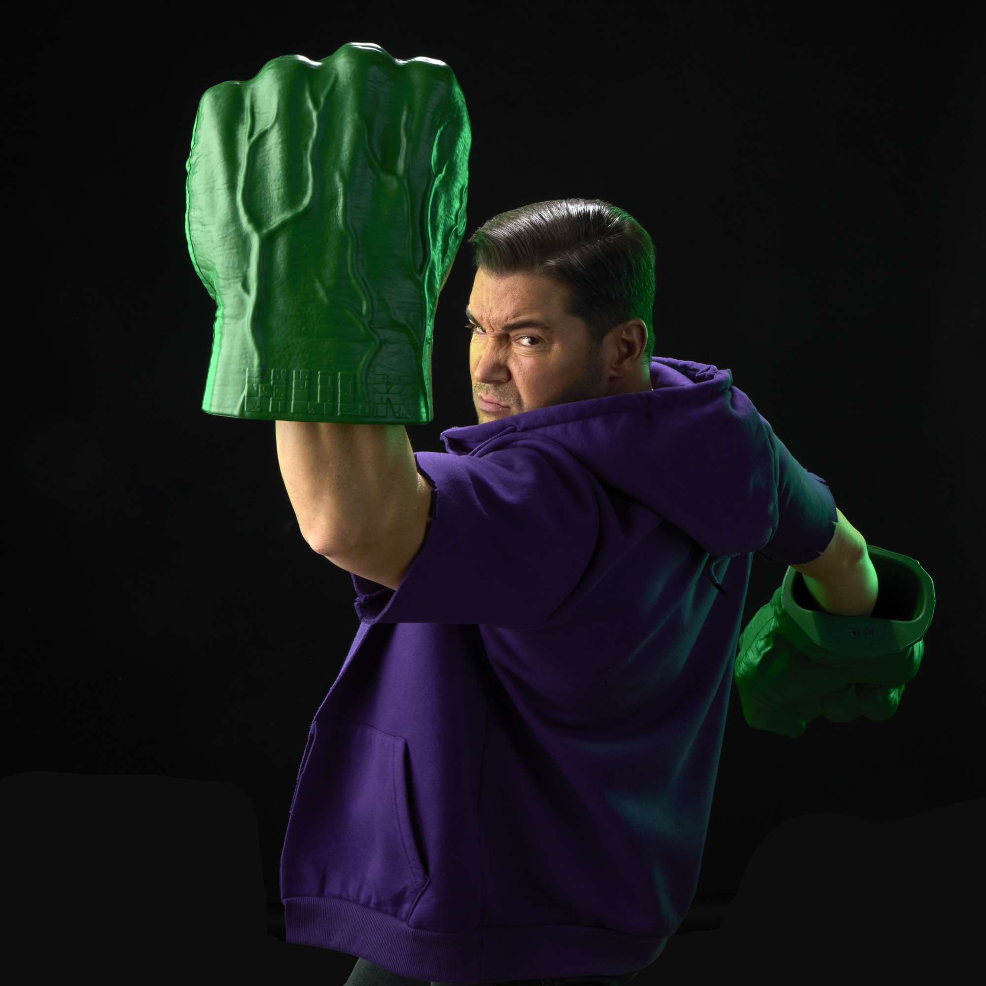 A roaring man with two Hulk Fists pretends to punch with them against a black background