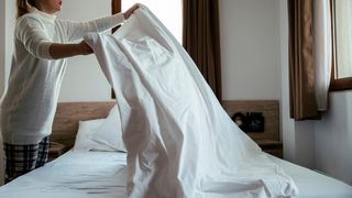 A woman making the bed in a using white bedding in a room