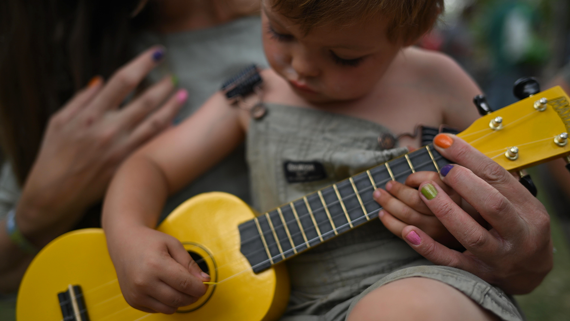 Three-year old Leo McKevitt plays a ukulele with his mother at the 36th annual Rocky Mountain Folk Festival in Lyons, Colorado