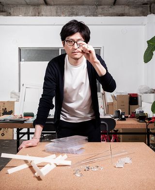 A portrait of designer Satoshi Yoshiizumi, founder of Takt Project, looking through a piece of crystal