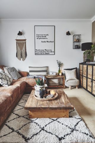 Living room with white walls, tan leather L-shape sofa, rugs, rattan pouffs and coffee table made from wooden palett boards