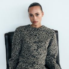 Zara model wearing cheetah print coat, sitting on black chair during studio photoshoot.