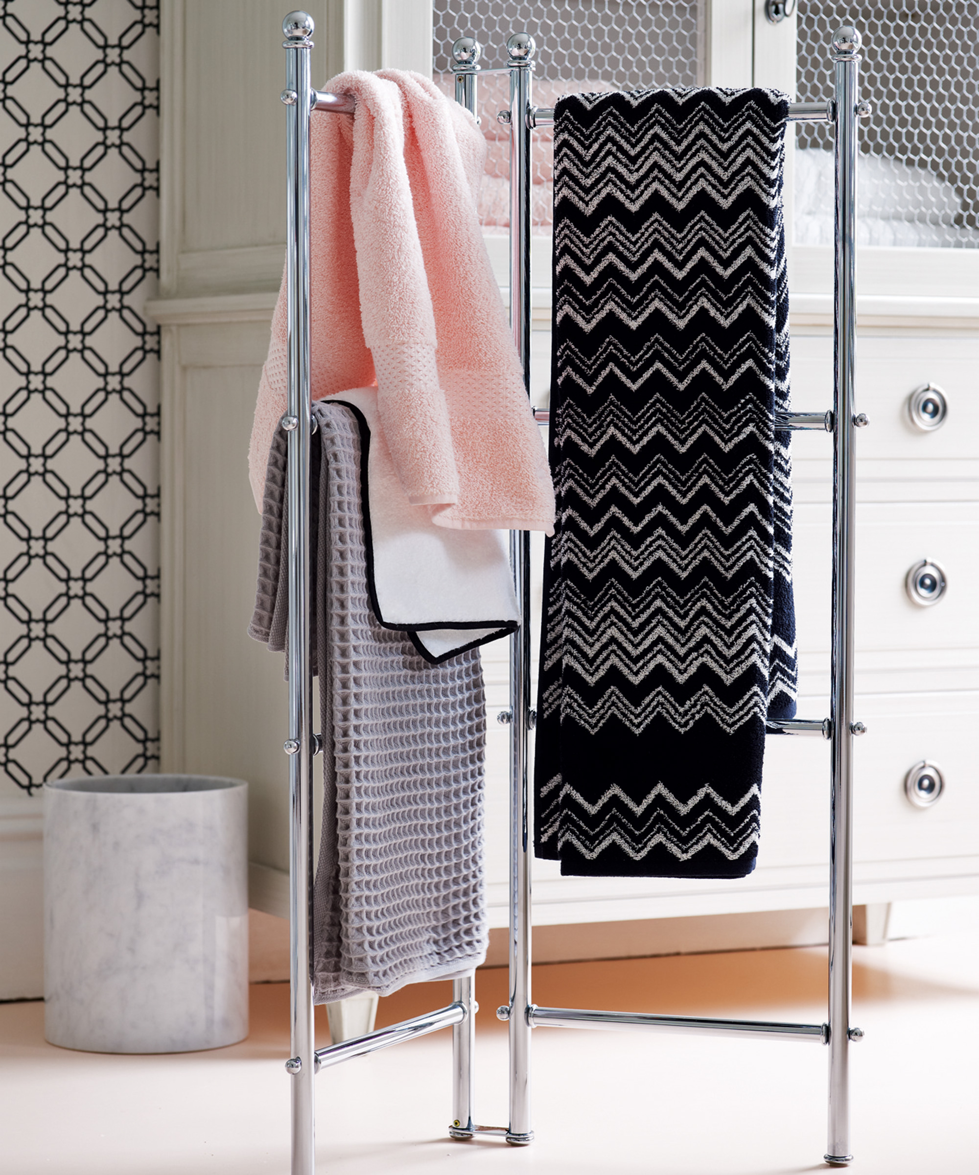 A heated bathroom towel rail with black and pink towels hanging on it in front of a storage unit