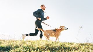 a photo of a man running with a dog by his side attached to a leash