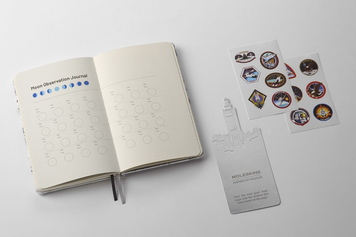 NASA-inspired Limited Edition Notebook from Moleskine showing off its "Moon Observation Journal" page to track moon phases. There is also a bookmark of rocket blasting off with an inspirational quote ("Even the most giant leaps begin with the smallest idea noted down on the page."), and 12 NASA/space-themed stickers.