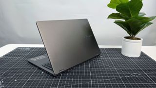 The Asus Vivobook 16 Flip convertible laptop facing away on a black and white desk against a gray background.