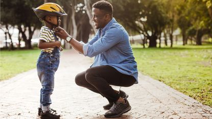 A dad helps his young son secure his bicycle helmet.