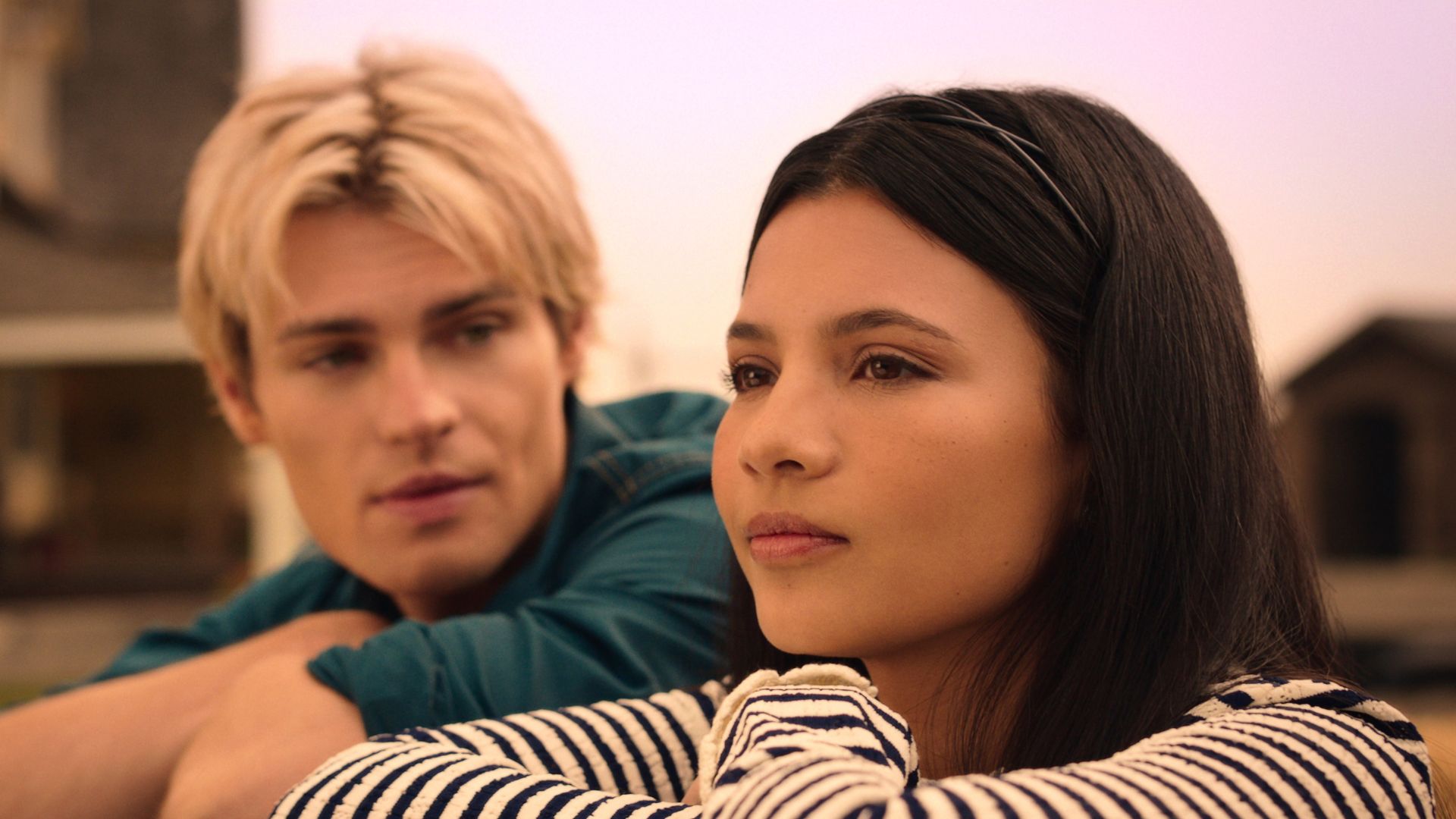 A blonde boy looks at a girl as she leans on a fence