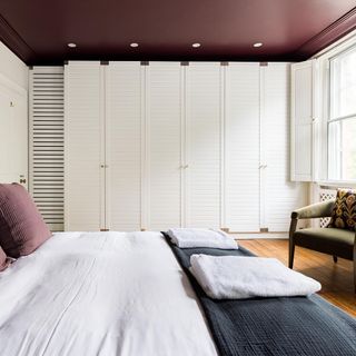 Bedroom with white cupboards on wooden floor and comfortable velvet green chair in corner