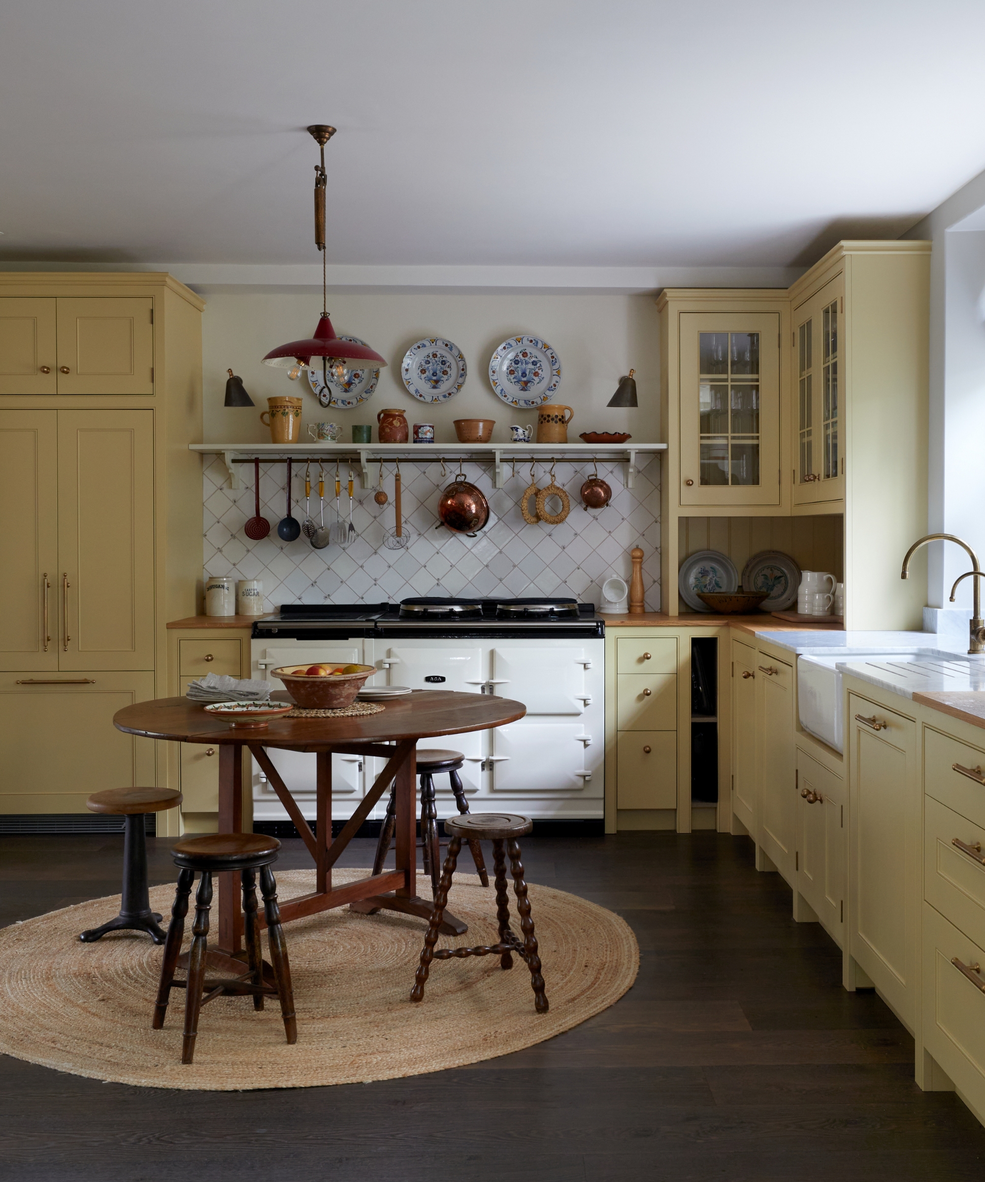 A kitchen with light yellow cabinets, dark wood floors, a wooden table, and a white aga