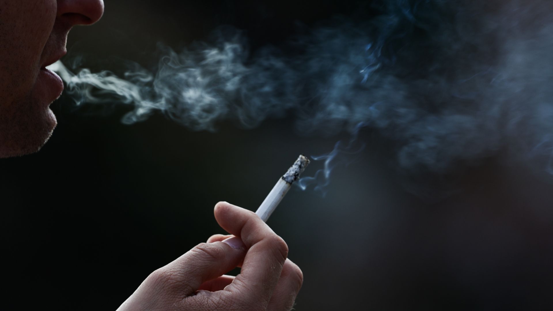 A close-up shot of a man smoking a cigarette at night.