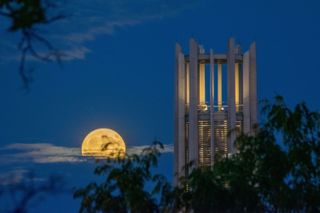 full moon rising through partly clouded skies next to a tall tower.