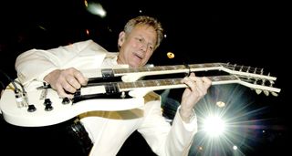 Don Felder plays his iconic white Gibson doubleneck electric guitar onstage. Note the double jack: that mod is crucial when playing Hotel California, which he surely is in this picture.