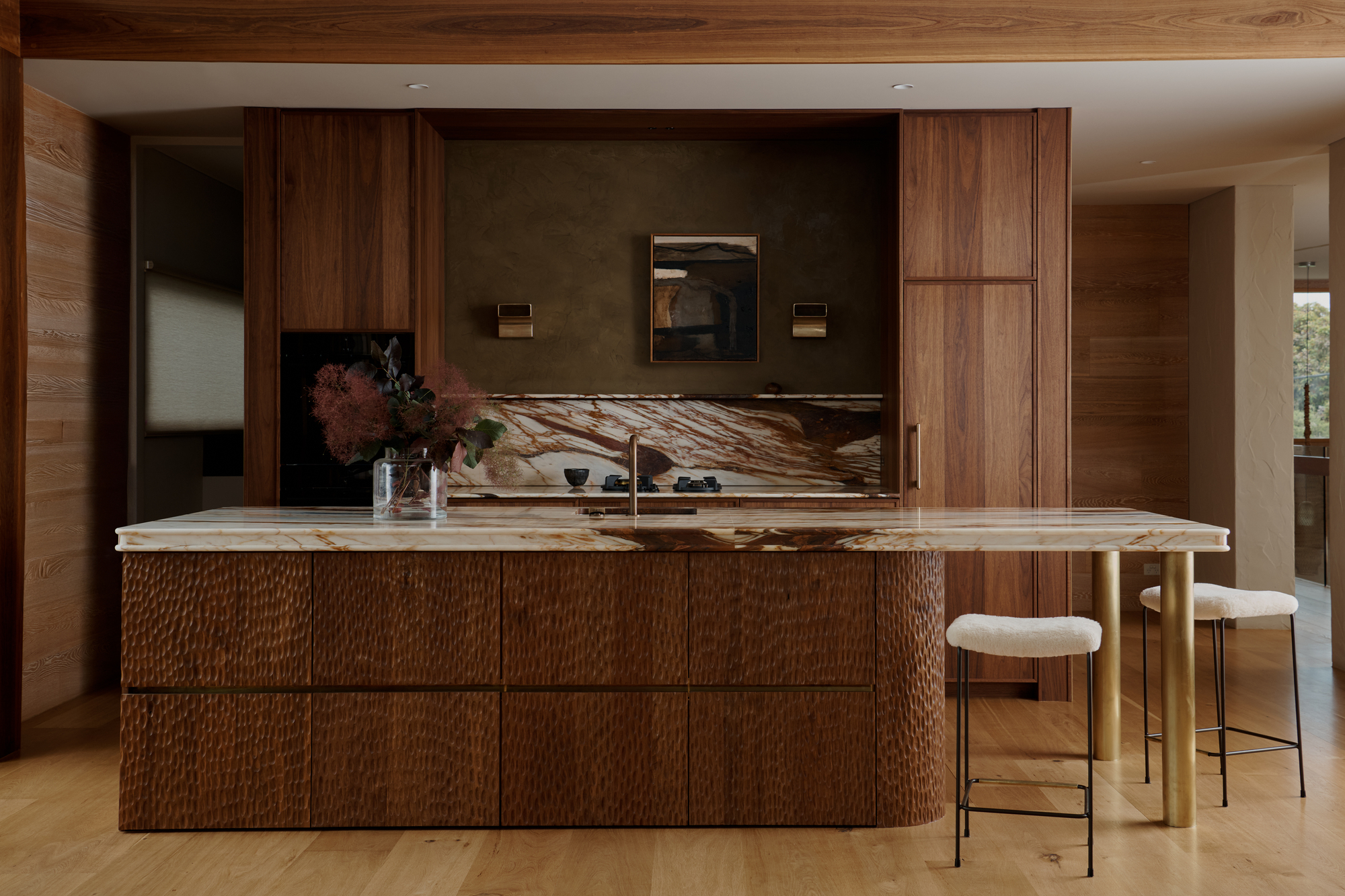 modern timber kitchen with dimpled-texture kitchen island, marble backsplash and countertop, brass taps, limewash wall in olive green, and boucle bar stools
