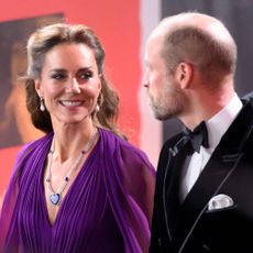 Kate Middleton arrives at the "Digger" Premiere wearing a royal purple long-sleeve maxi dress with a long necklace and drop earrings. She walks alongside Prince William.