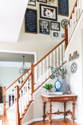 Entryway with gallery wall up the stairs, wooden bannisters, and a wooden table with a vase, clock and plant