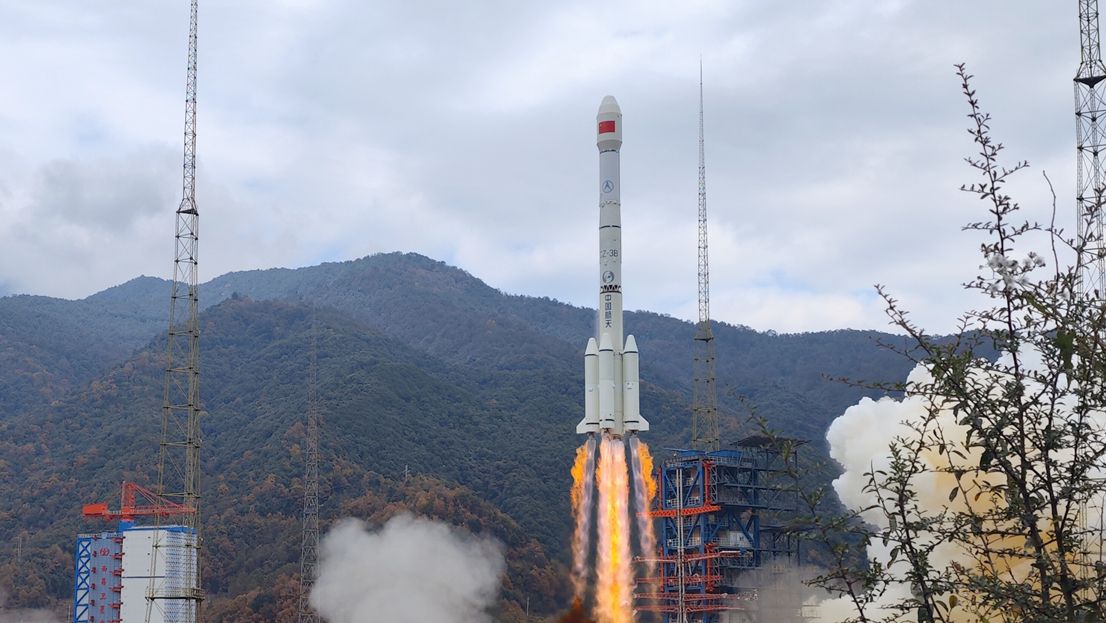 a white rocket launches into a cloudy sky, with forested hills in the background