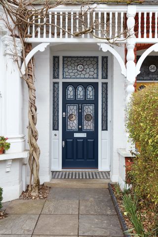 a blue Victorian front door with glazed panels, with white structure around it, at the end of a paved path