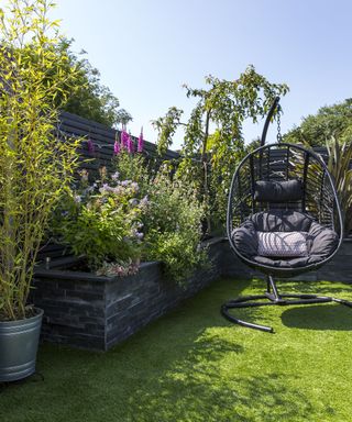 A hanging egg chair on an artificial lawn with raised beds and low maintenance planting