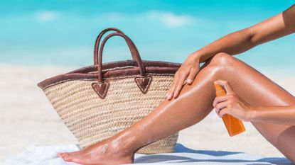woman using a spray sunscreen on the beach