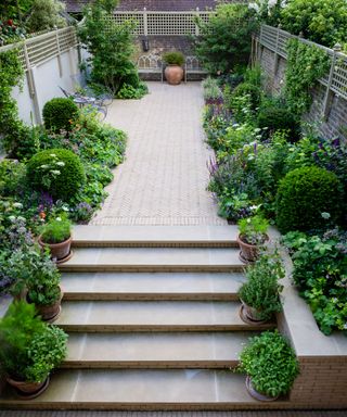 narrow small garden with wide steps and herringbone paving with raised borders in design by Butter Wakefield