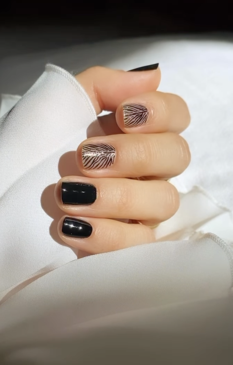 Short square nails with glossy black polish and two sheer accent nails featuring thin black zebra stripes