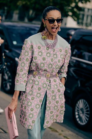 A smiling woman wearing a floral blazer, flower belt, choker necklace, and matching earrings