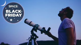 Man uses telescope to look at moon with blue sky behind
