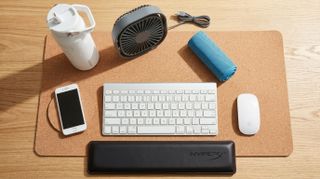 A water bottle, cooling scarf, keyboard, USB fan, desk mat, and wrist rest in a very bright, warm home office
