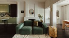A living room with art deco influence featuring a green sofa, a textured rug, a burl wood side table and a mirror