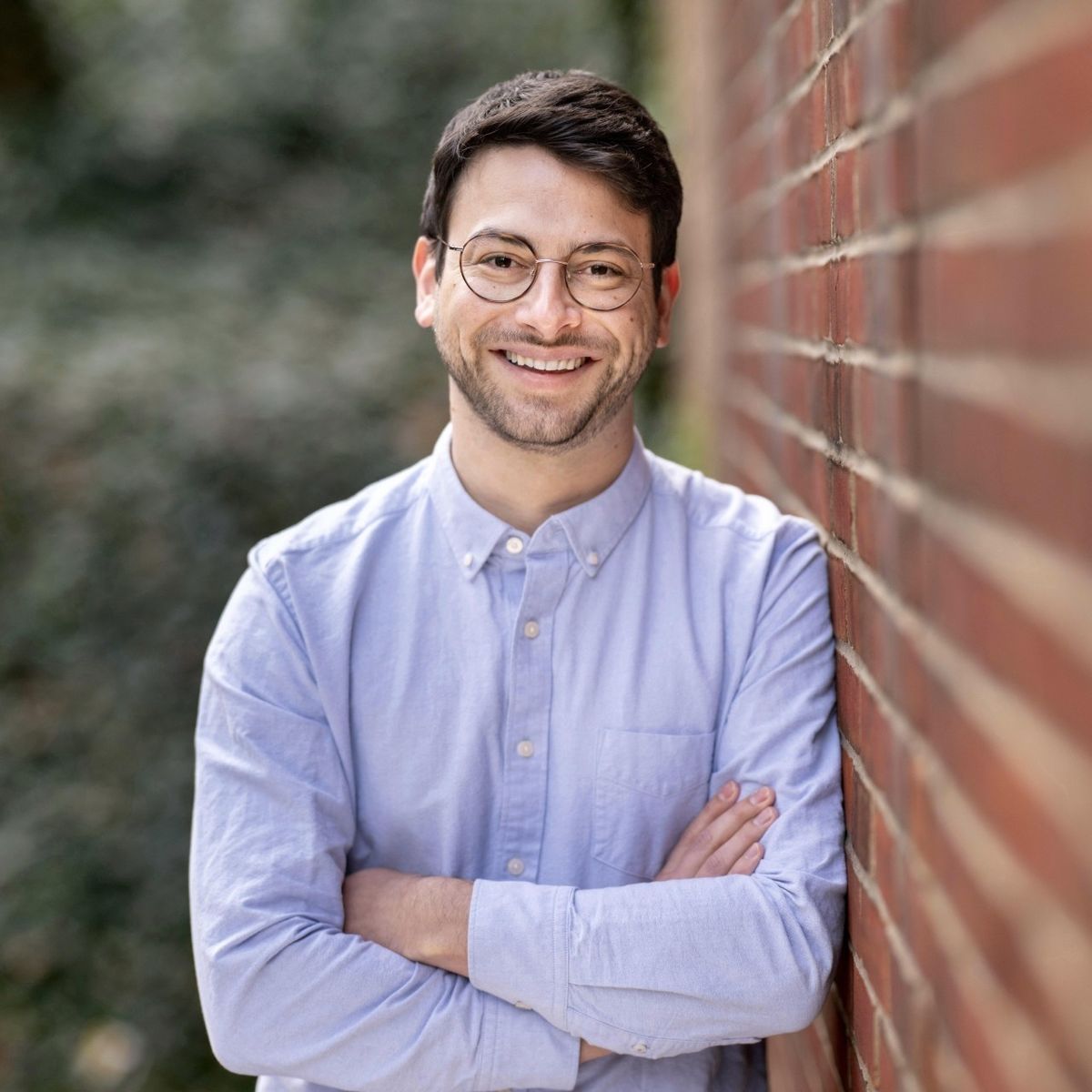 photo of smiling man with short brown hair, glasses and a button up shirt