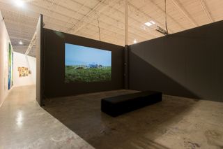A video exhibition space inside the area with a bench and an image of a field on a wall titled Videos 2000- 2009.