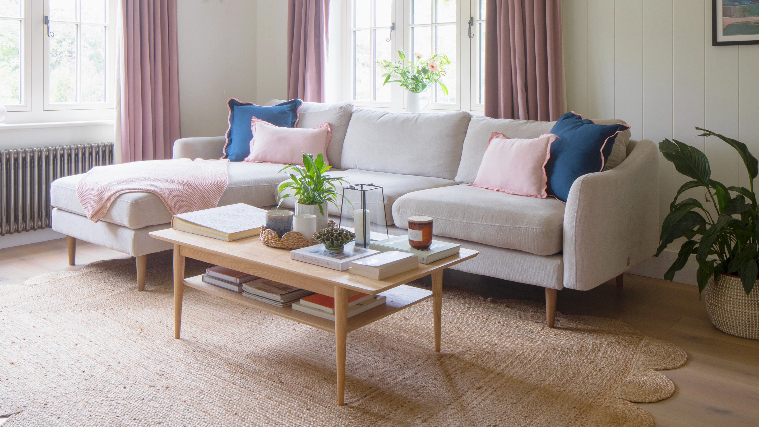 A living room with a chaise light grey sofa positioned a few inches away from the wall with a scalloped jute rug on the floor