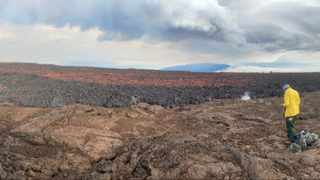 A member of the Hawaiian Volcano Observatory field crew is pictured taking notes from the summit of the volcano