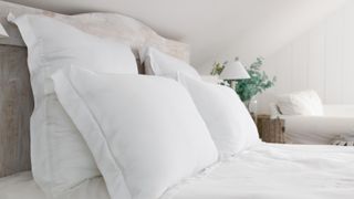 image of a white bed with white cushions and pillows, with a beige headboard and a nightstand in the distance, from Ethical Bedding