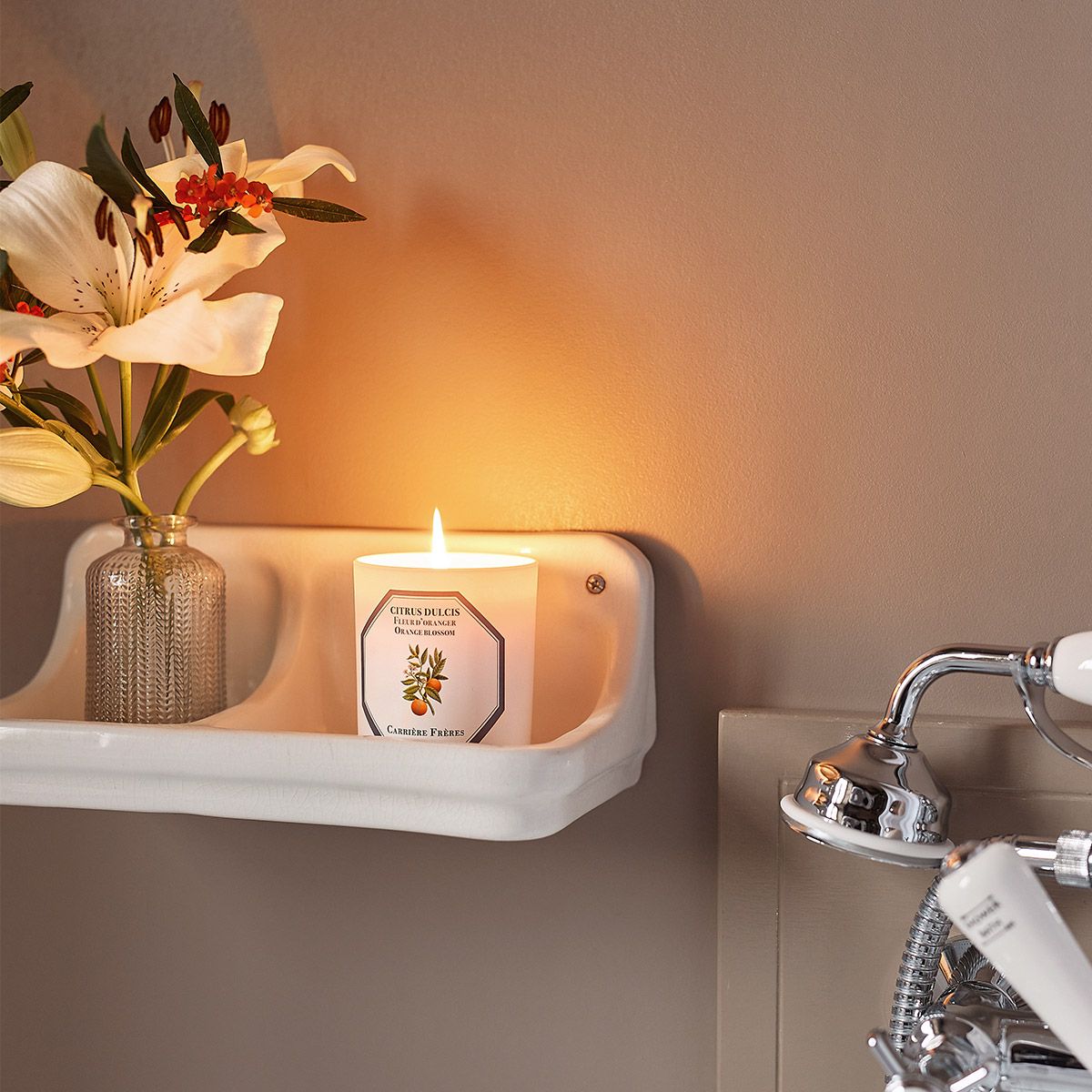 candle beside bathtub in a tray next to a lily in a vase