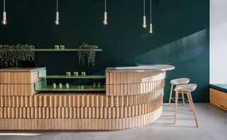 A bar counter made of cream bricks with a grey top, wooden bar chairs and globes hanging above it.