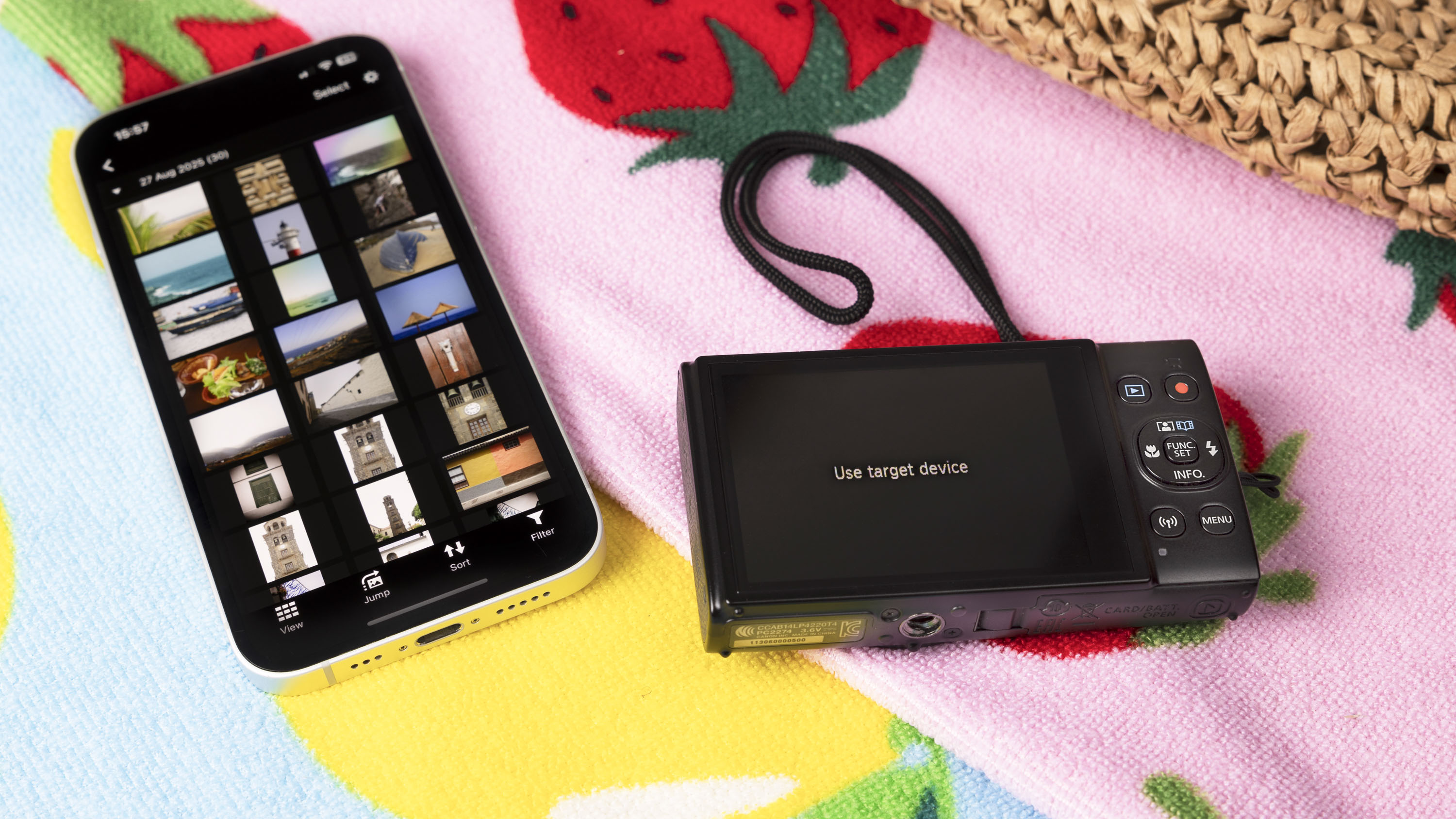 Canon PowerShot Ixus 285 HS A point and shoot camera in black, on a bright beach towel, alongside phone with the Canon app