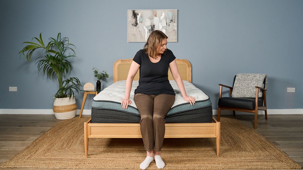 Tester Ruth Jones sits on the side of the Helix Sunset Luxe Mattress to test its edge support.