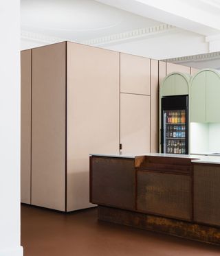 Close up view of the bar area at Yorck Kino Passage cinema featuring brown floors, a brown bar counter, a black fridge, pastel pink units and arched pastel green units