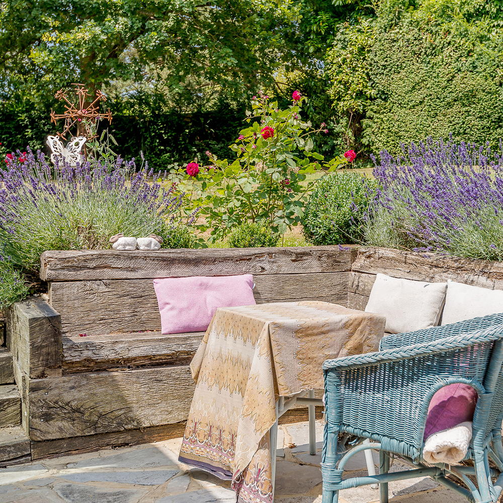 Wooden sofa, coffee table and wicker chair in garden with lots of flowers