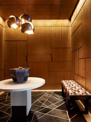 Entryway with wood panelling, black geometric rug and brass lighting