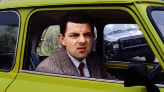 Mr bean making a grimace as he gazes out of a Taxi