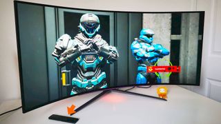 LG UltraGear Ultrawide monitor with Halo Infinite Spartans on screen and orange arrow pointing to remote control sitting on left hand side.