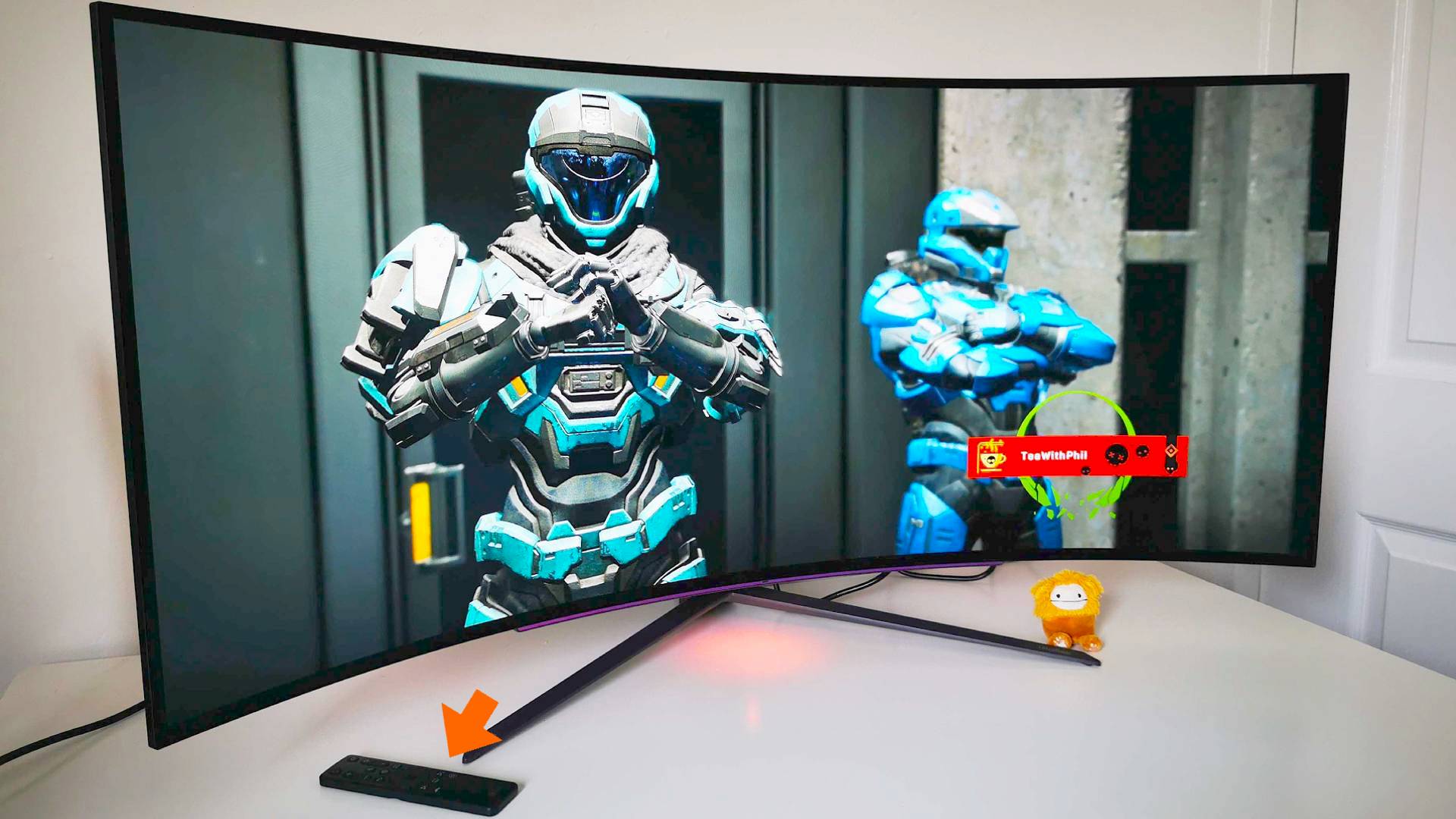 LG UltraGear Ultrawide monitor with Halo Infinite Spartans on screen and orange arrow pointing to remote control sitting on left hand side.