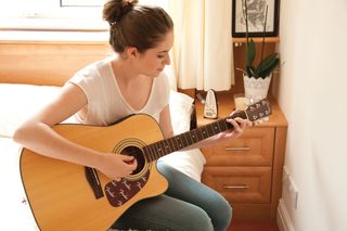 Woman playing acoustic guitar to a metronome