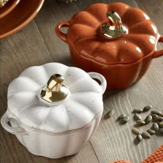 White and orange pumpkin shaped mini hot pots on wooden table 