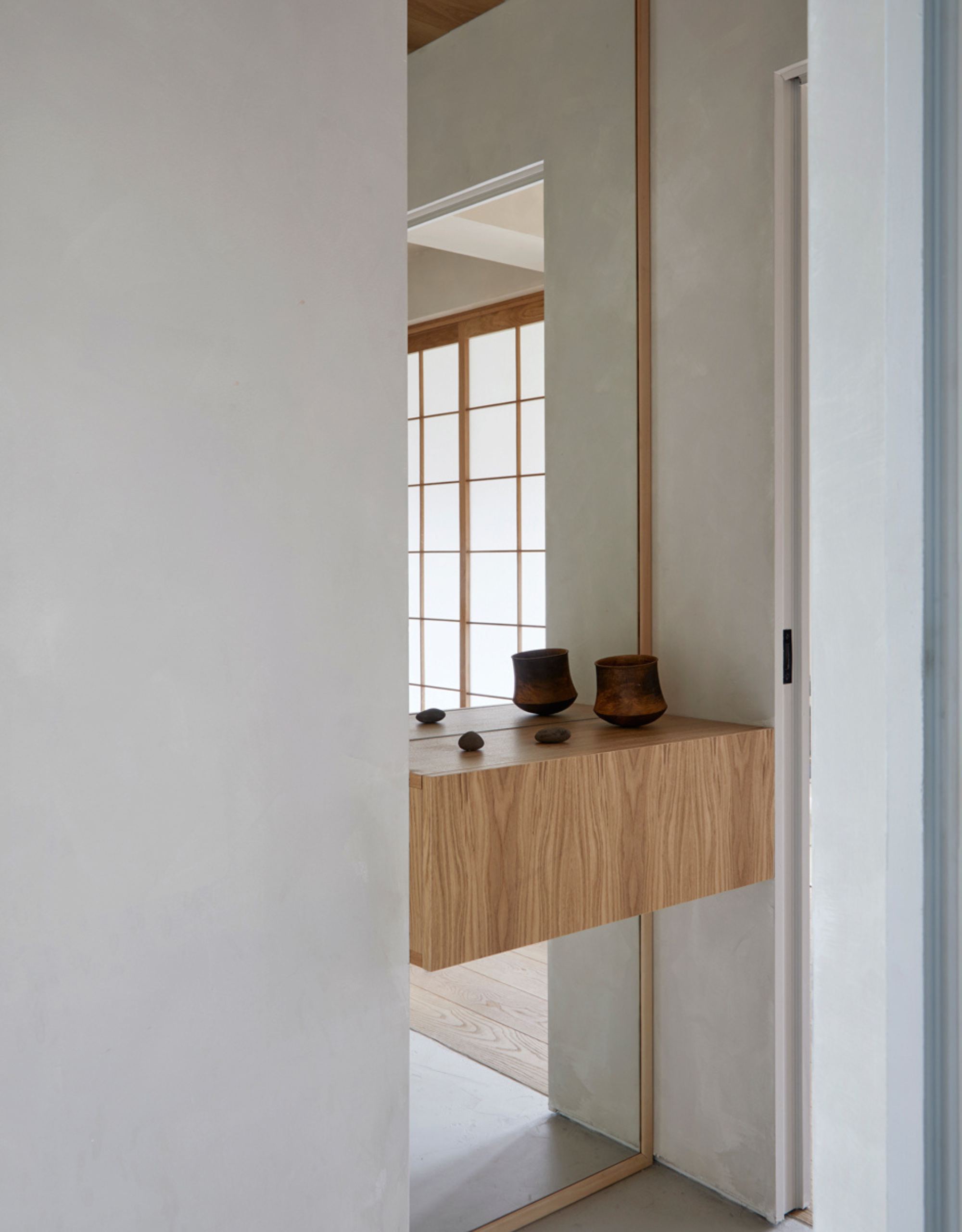 A wooden counter with brown ceramics in a white room with a mirror