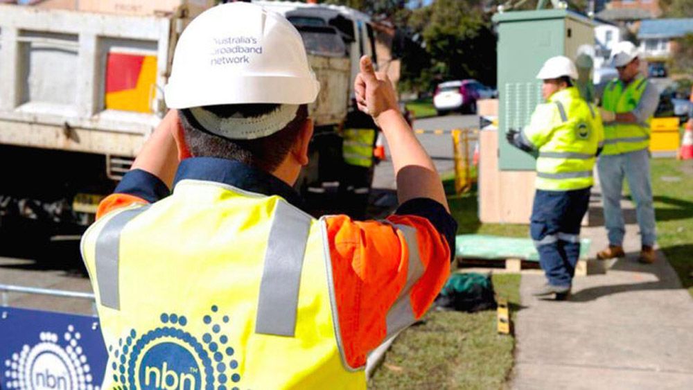 An NBN technician giving a thumbs up to other technicians further down a street.