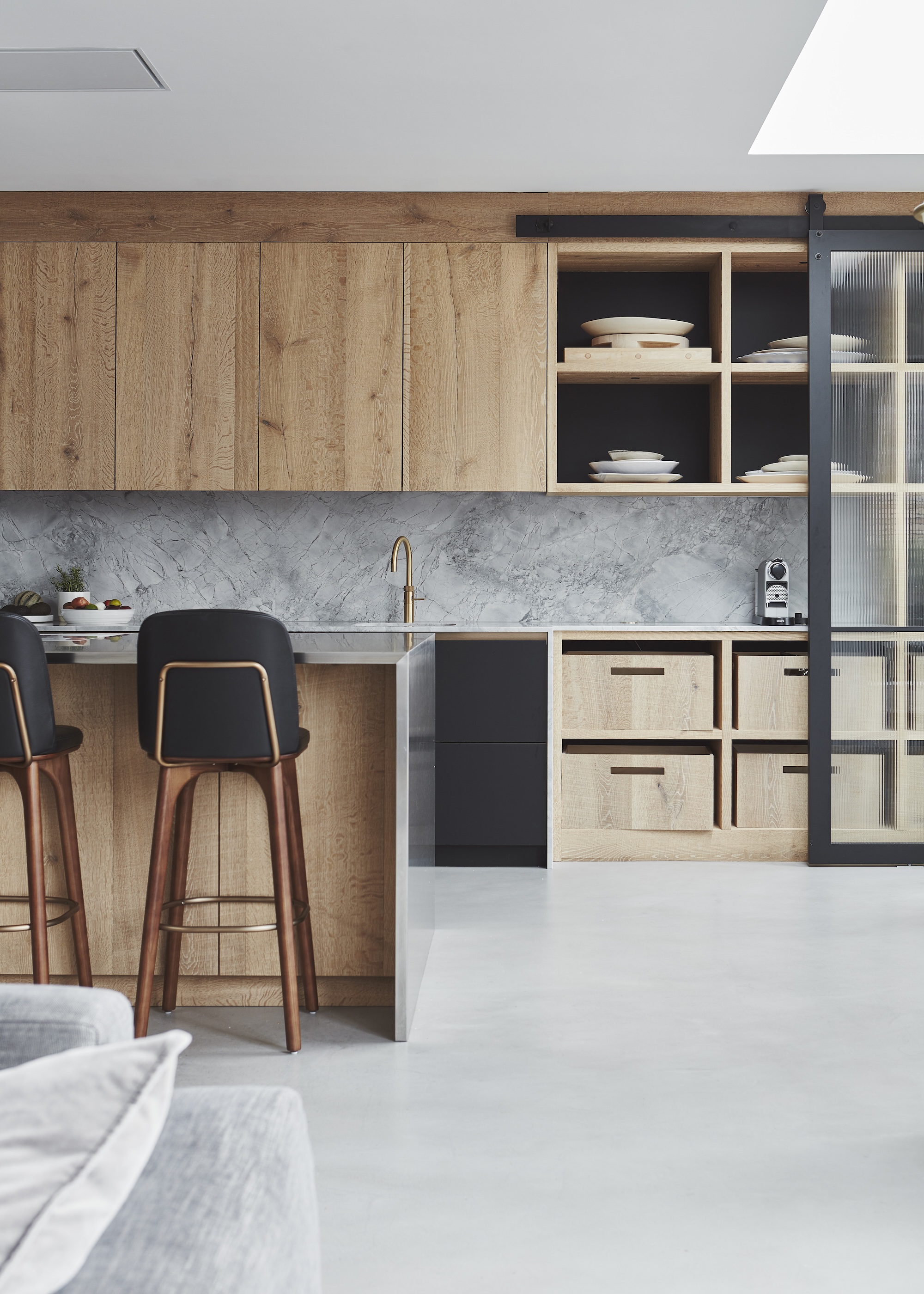 A kitchen with open shelving and closed storage units. The kitchen also has an island in the middle with bar stools beside it.